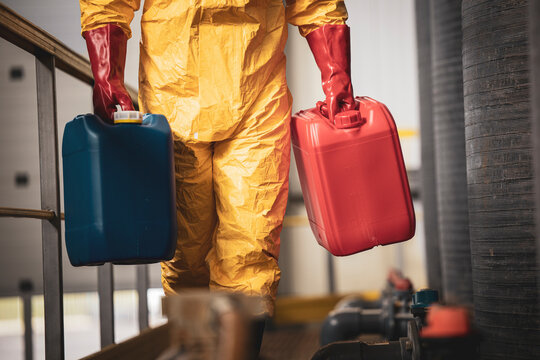 Unrecognizable chemicals worker carrying plastic canisters inside factory.