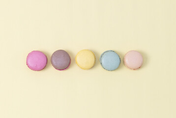 Five colorful macaroons on a yellow background.