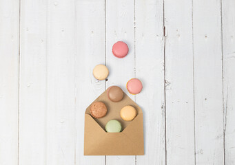 Macaroon falling out of an envelope on a white wooden table.