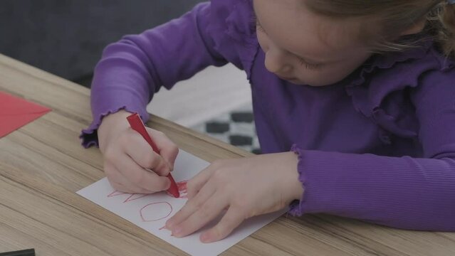 portrait of creative liitle toddler girl drawing a surprise card for mother, coloring with red heart shapes on paper