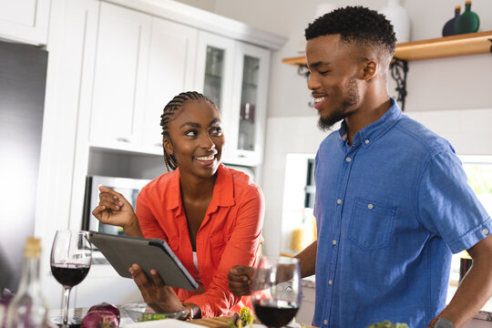 Happy african american couple cooking dinner together, using tablet in kitchen