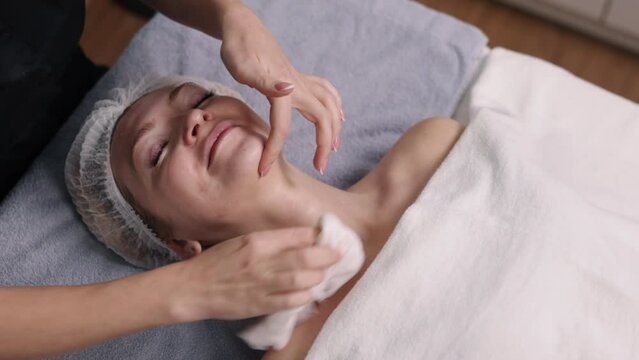 client's face, Removing mask, beautician wipes off. Beauty studio, beautician wipes off remaining mask from face of client using napkin, cosmetologist washes off nourishing mask from face of patient