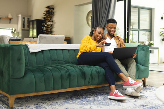 Happy african american couple sitting on sofa and using laptop for online shopping, copy space