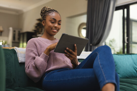 Happy african american woman sitting on sofa and using tablet in living room