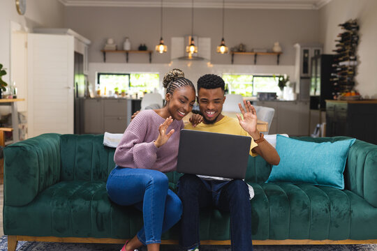 Happy african american couple sitting on sofa and using laptop for video call in living room
