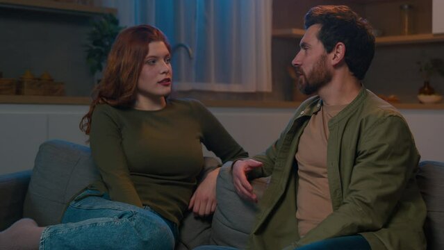 Upset married caucasian couple man and woman with relationship problems talking sitting on sofa evening in kitchen frustrated husband speak offended serious wife listening family conversation at home