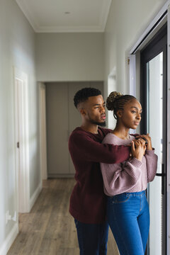 Happy african american couple looking through window and embracing