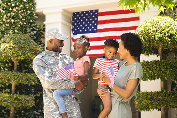 Happy african american soldier and his family embracing, holding usa flags