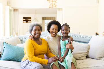 Portrait of happy african american grandmother, mother and daughter sitting on sofa in living room