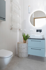 Luxurious and interior of bathroom with ceramic washbasin on the cabinet, round mirror o the white wall with led lights and toilet. Vertical.
