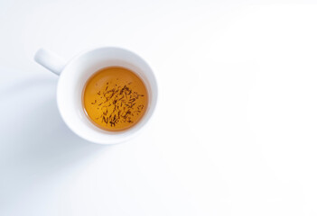 top view of a white tea cup on a white background with some tea infusion and tea grounds in the...