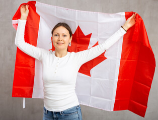 Happy young woman with large flag of Canada posing gladly against light unicoloured background