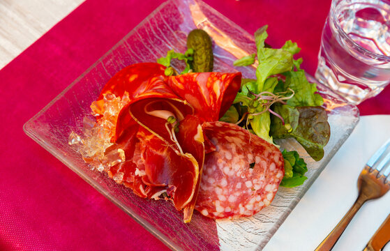 Appetizing assorted meat of smoked sausage and sliced carbonad, served with pickled cucumbers and lettuce