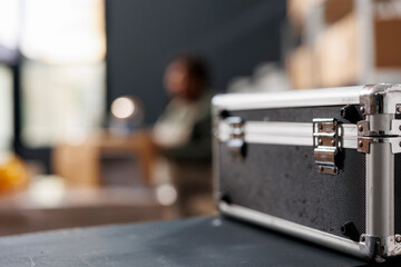 Selective focus of metallic silver box standing on counter desk in storehouse, in background african american employee preparing clients packages. Stockroom manager working at merchandise inventory