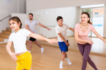 Girl dancing modern dance with family during group rehearsal in gym.
