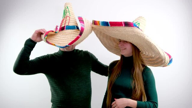 man and woman in big mexican sombrero hats white background in green sweaters smiling leaning to side travel entertainment waiting for vacation to travel agency want to go to mexico cancun