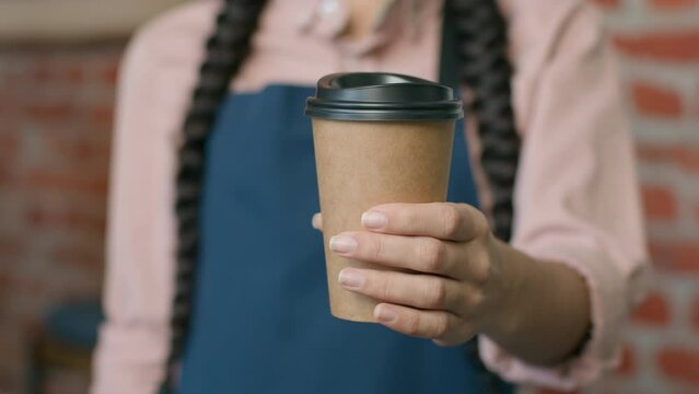 Close-up unrecognizable woman barista waitress in apron holding disposable paper cup with hot coffee or tea female small business owner cafe restaurant coffee house serving drink takeaway food concept