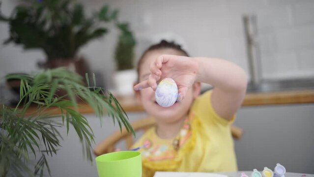 Child girl of preschool age painting Easter eggs at home kitchen. Easter spring traditions. Slow motion