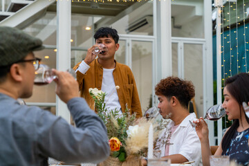 Group of Asian people eating food and drinking wine together during outdoor celebration dinner party in the garden on summer holiday vacation. Man and woman friend reunion dining meeting at restaurant