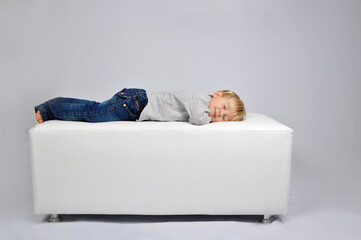 criança feliz sonhando deitada confortavelmente em sofá descansando  - obrazy, fototapety, plakaty