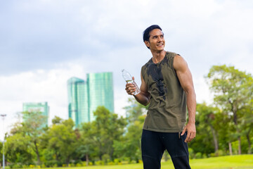 Asian man in sportswear drinking water from a bottle during jogging exercise at public park in the morning. Healthy guy athlete enjoy outdoor lifestyle sport training workout running in the city.