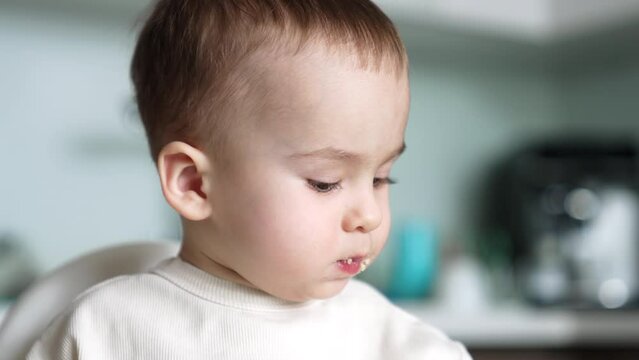 Beautiful infant kid having meals. Child with smudged face close up. Baby boy is fed from spoon.