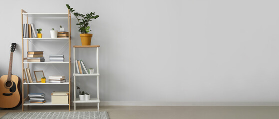 Shelving unit with books, houseplants and guitar near light wall in room. Banner for design