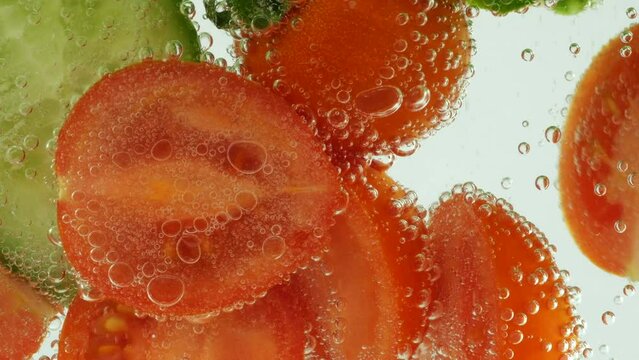 Slices of fresh cucumbers and tomatoes in clear water