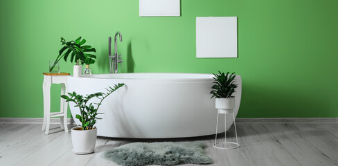 Obraz na płótnie Canvas Modern bathtub with houseplants near green wall