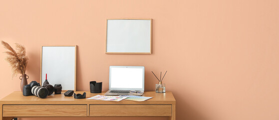 Photographer's workplace with laptop, modern devices and blank frames near beige wall. Banner for design