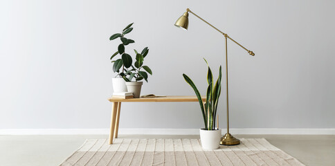 Bench with houseplants, books and standard lamp near light wall in room