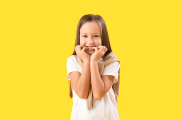 Little girl biting nails on yellow background