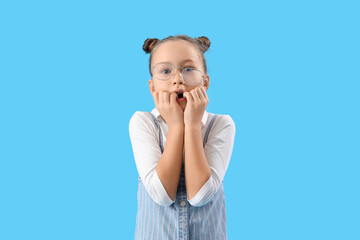 Stressed little girl biting nails on blue background