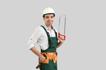 Young carpenter with hacksaw and hammer on grey background