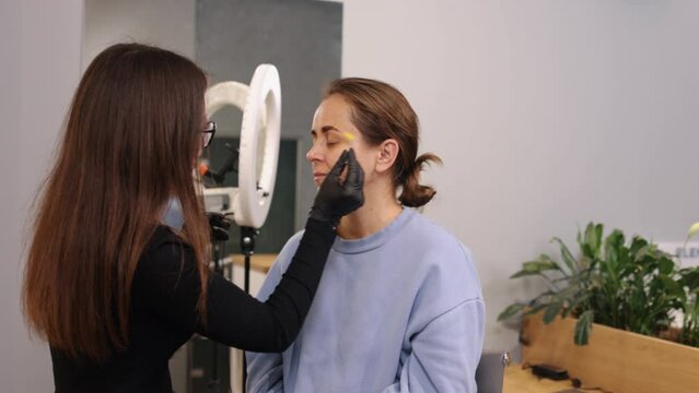 Brow shape, Beauty specialist, Eye makeup. Young woman is getting her eyebrows shaped and colored at beauty salon to enhance appearance.