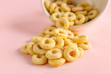 Overturned bowl of yellow cereal rings on pink background, closeup