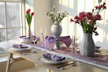 Beautiful table setting for International Women's Day celebration with different flowers and burning candles in light room near window