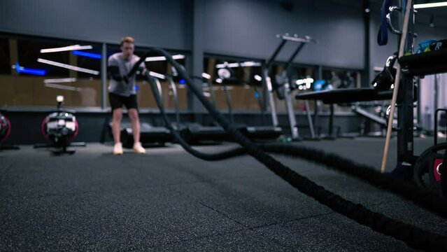 Fitness man exercising with battle ropes in a modern gym
slow motion