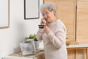 Senior woman with credit card talking by telephone at home
