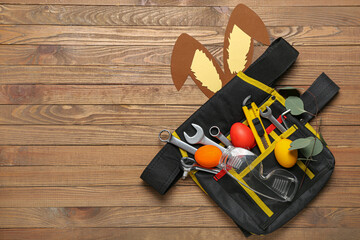 Bag with construction tools, Easter eggs and paper bunny ears on wooden background