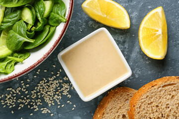 Bowl of tasty salad, tahini, bread and lemon slices on dark background, closeup