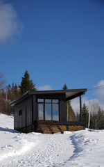 Front view of black modern wooden cabin on snowy mountains