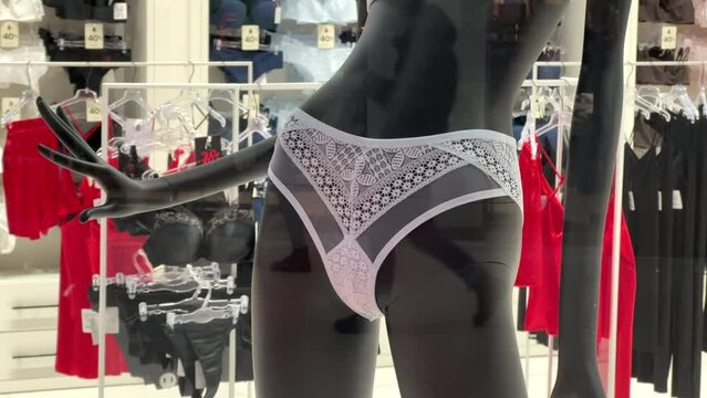 Women's transparent lace white panties are worn on a slender black mannequin in a lingerie shop window