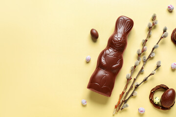 Chocolate Easter bunny with eggs and willow branches on yellow background