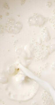 4K footage vertical video Top view SLO MO CU, milk being poured into a container making lots of bubbles.