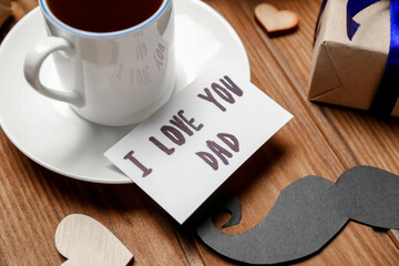 Cup of coffee, paper mustache and card with text I LOVE YOU DAD on wooden table, closeup. Father's Day celebration