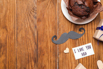 Tasty muffin, paper mustache and card with text I LOVE YOU DAD on wooden background