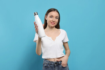 Beautiful young woman with thermos bottle on light blue background - obrazy, fototapety, plakaty