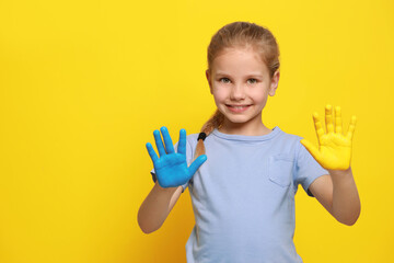 Little girl with hands painted in Ukrainian flag colors on yellow background, space for text. Love Ukraine concept