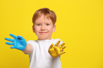 Little boy with hands painted in Ukrainian flag colors on yellow background, space for text. Love Ukraine concept